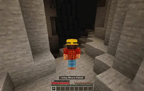 Игрок в шахтерском шлеме исследует темную пещеру в Майнкрафт ПЕ (Бедрок)